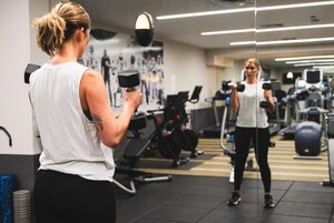 Un gimnasio con equipo de ejercicio, un espejo y una persona levantando pesas.