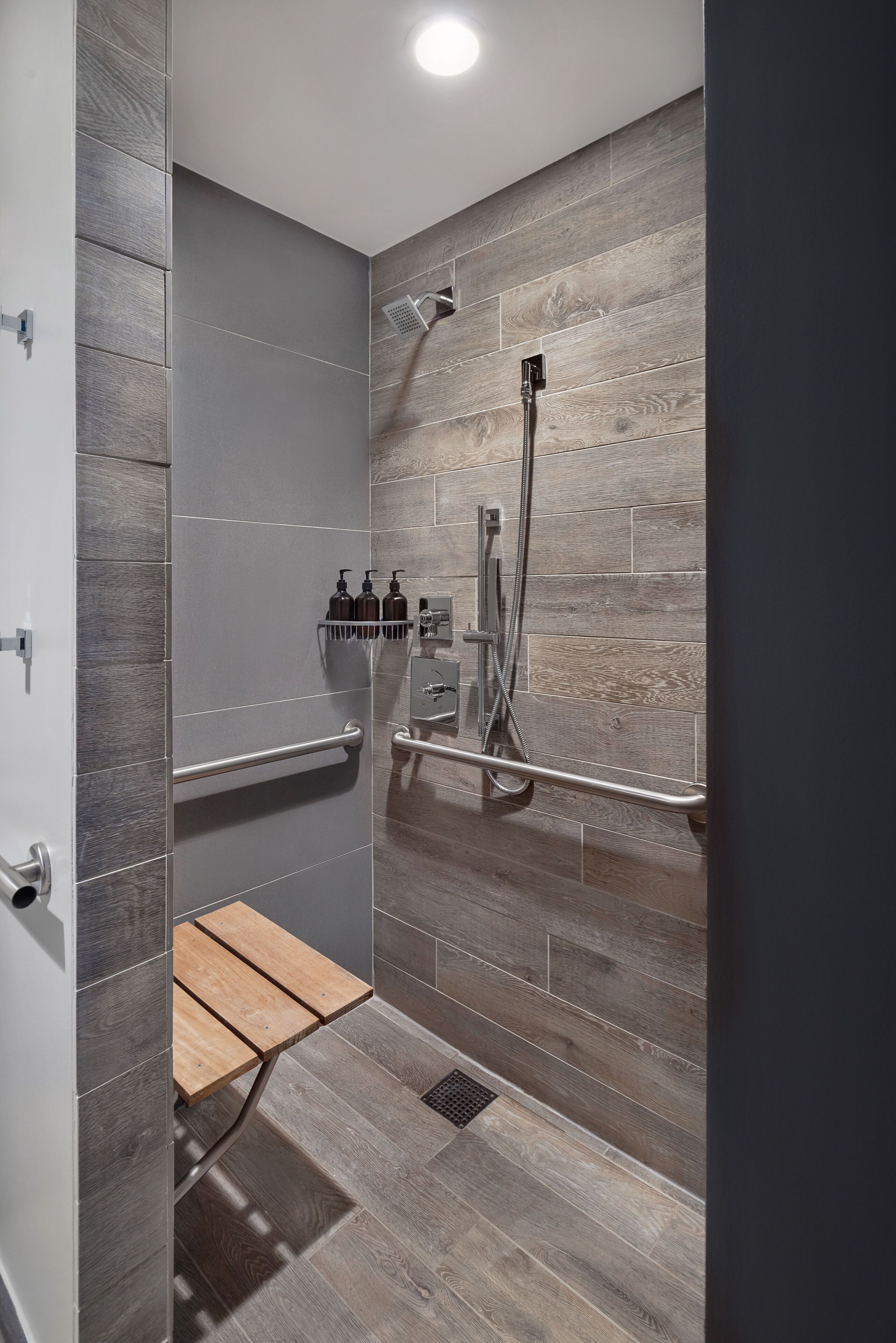 A modern shower with a wooden wall panel, a handheld showerhead, and a handheld faucet.