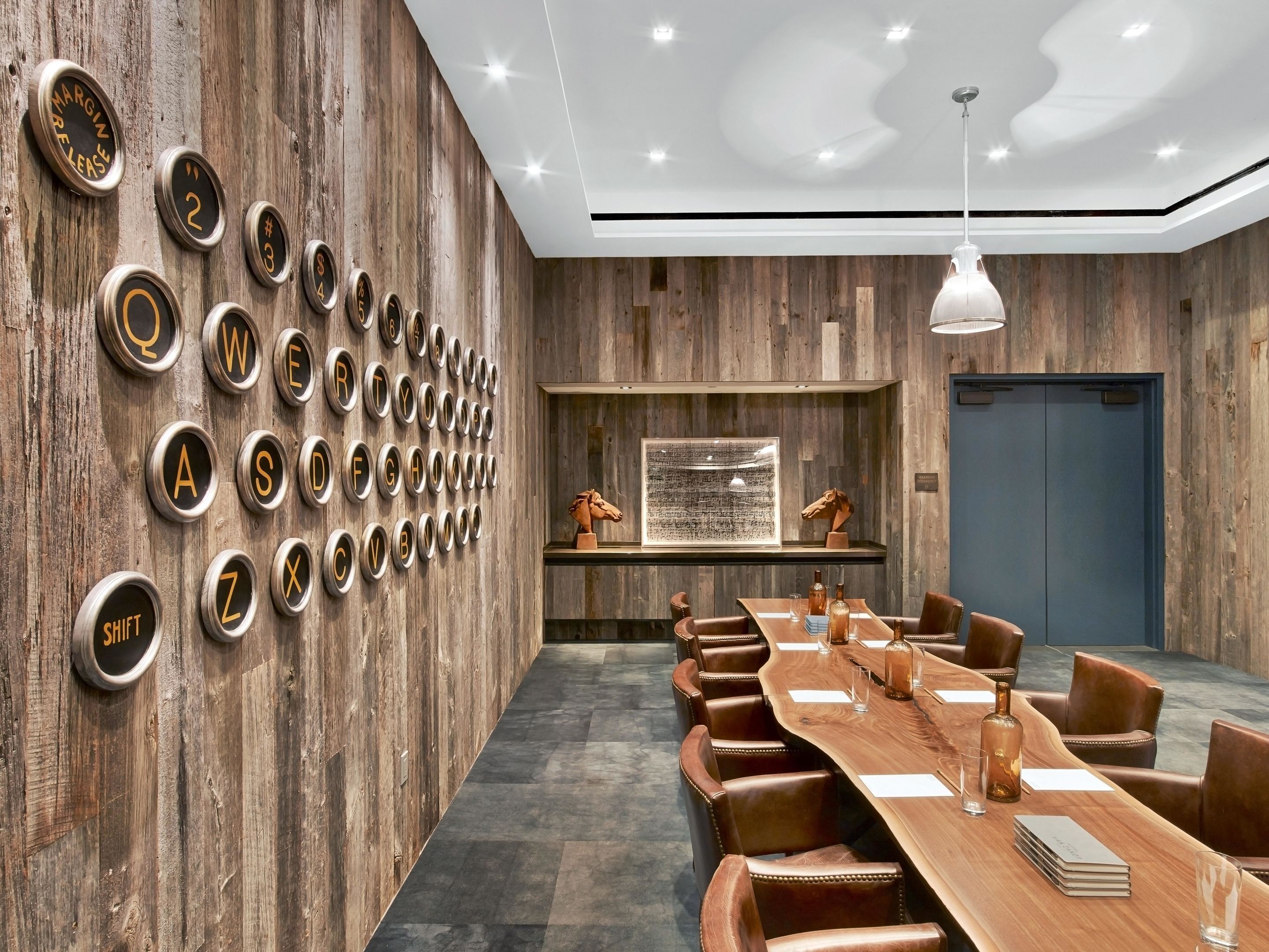 A conference room with a long wooden table, leather chairs, a mounted alphabet wall, and a mounted sculpture.