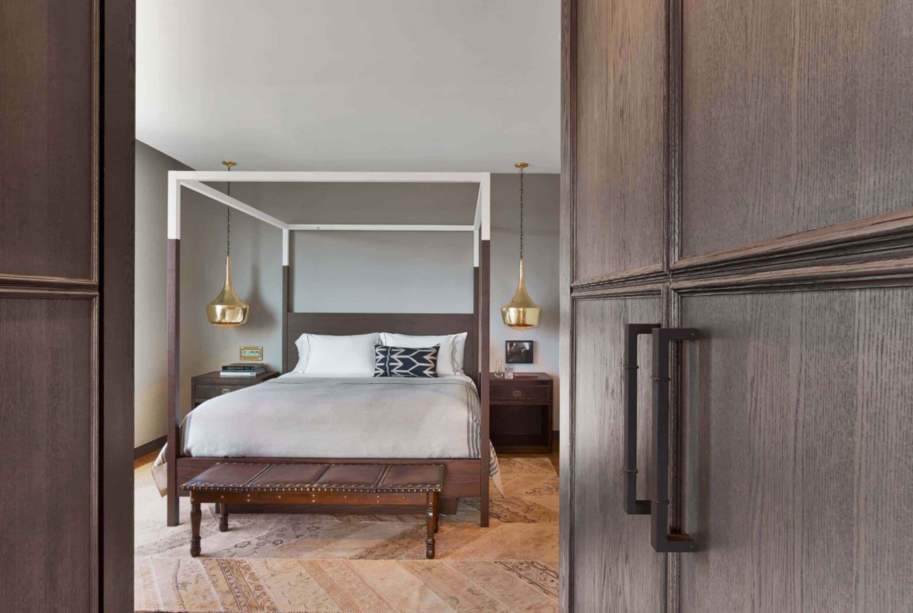 A bedroom with a four-poster bed, a bench, two bedside tables, and a hanging light fixture.
