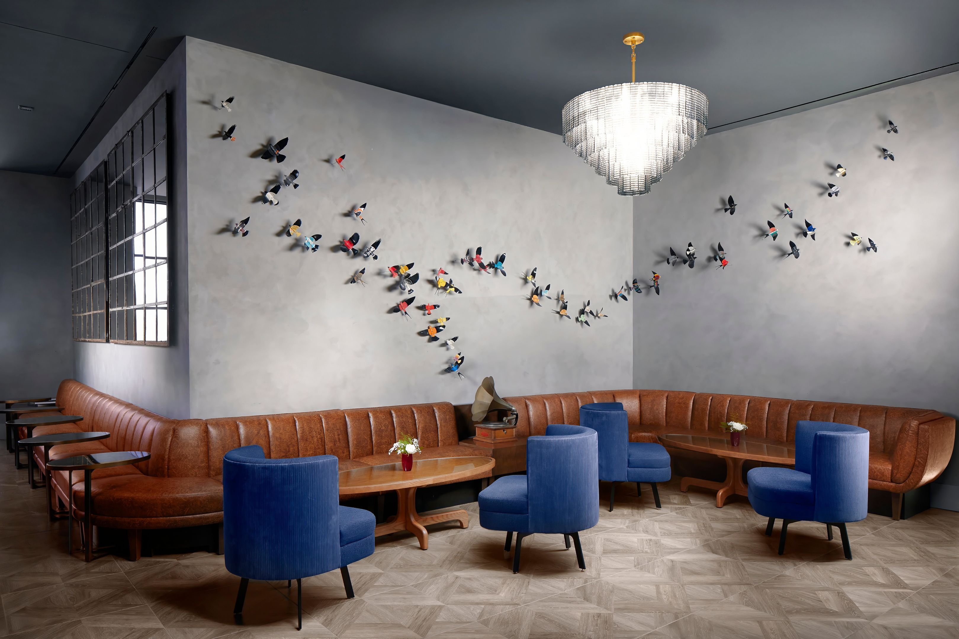 A modern lounge with a curved bench, blue chairs, a wooden table, and a wall decorated with butterfly art.