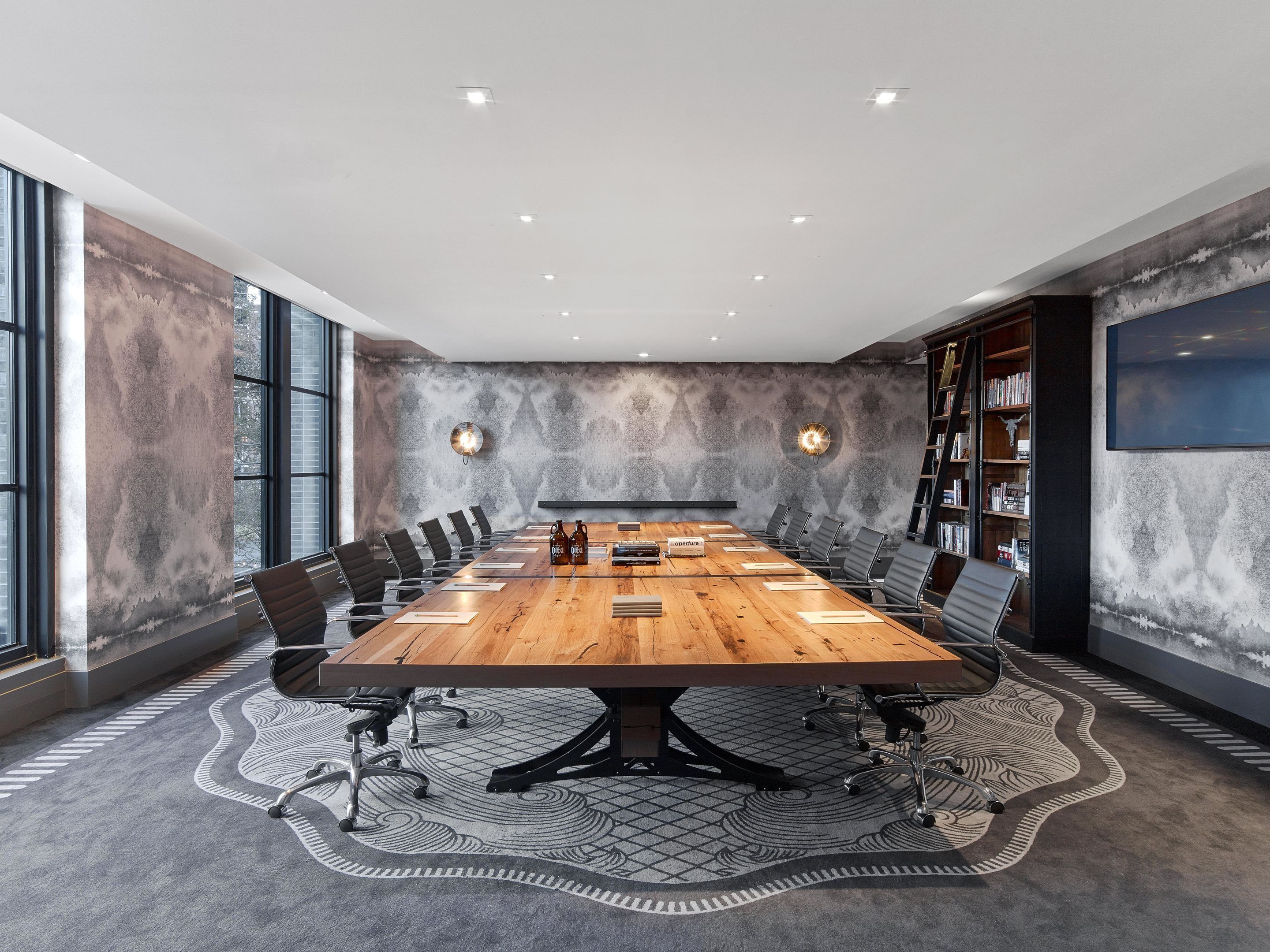 Uma sala de conferências com uma grande mesa de madeira, cadeiras pretas e um tapete estampado.