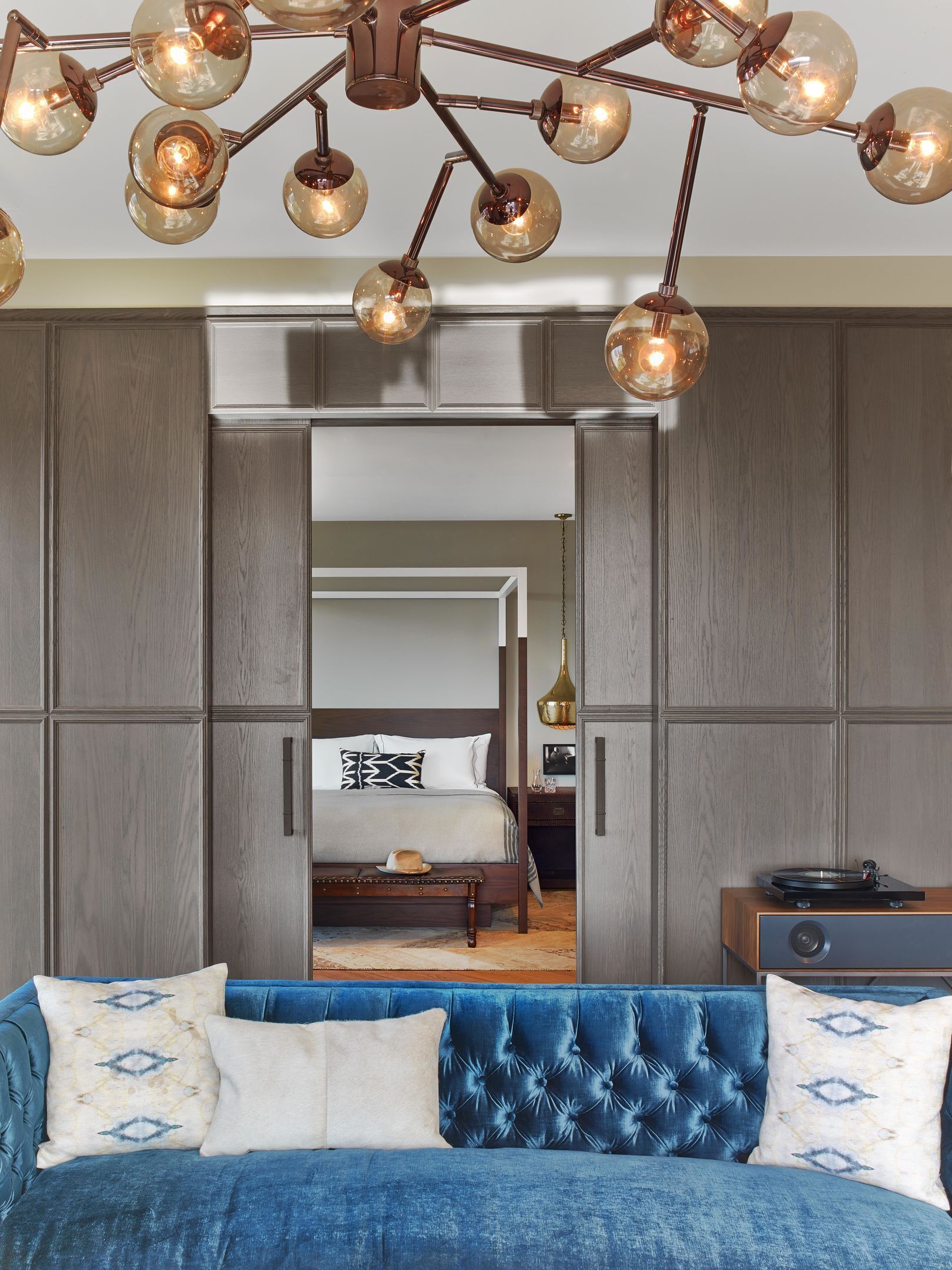A bedroom with a large bed, a blue upholstered sofa, a modern chandelier, and a wardrobe.