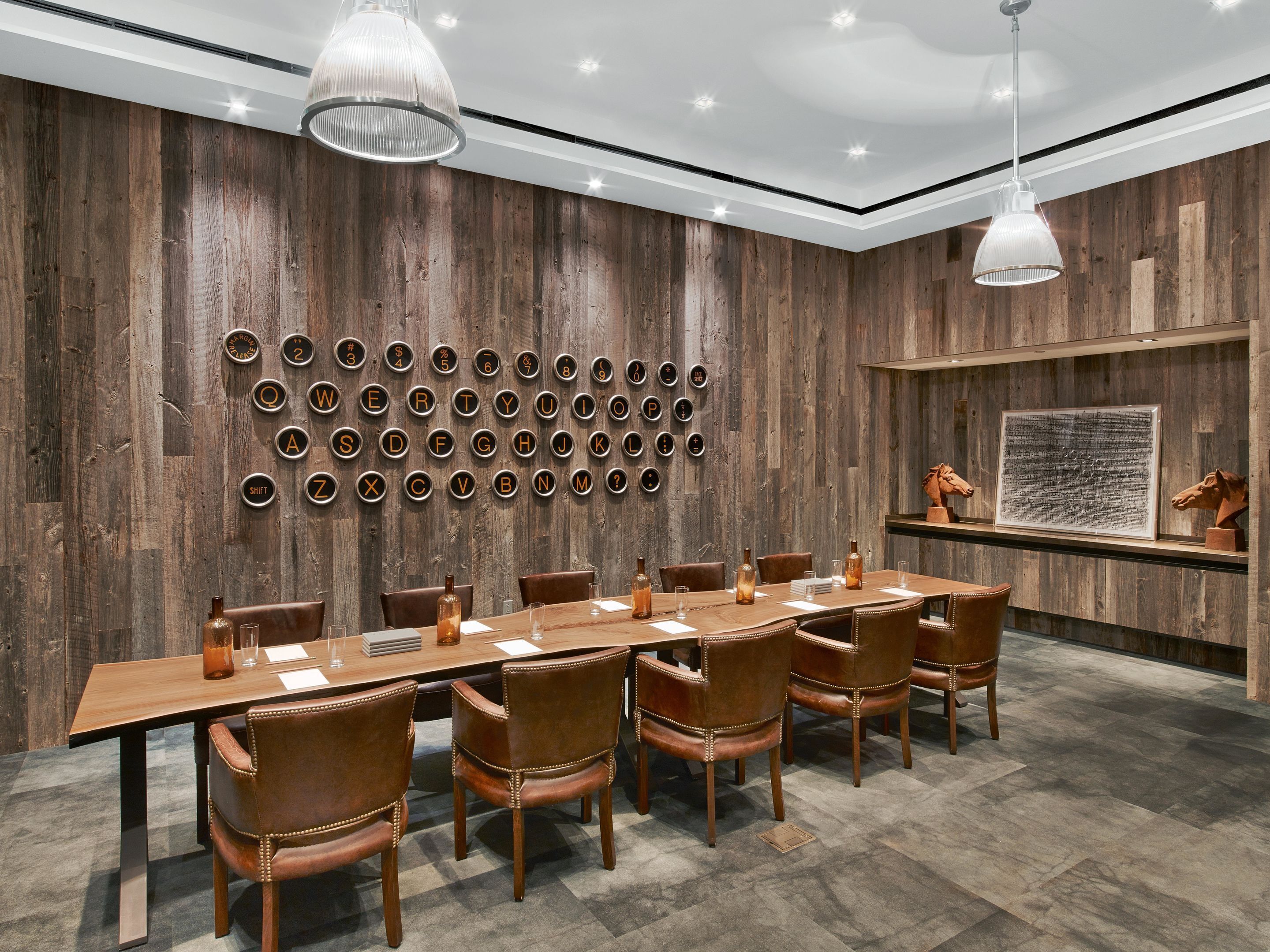 A conference room with a long table, leather chairs, a wooden wall with alphabet letters, and pendant lighting.