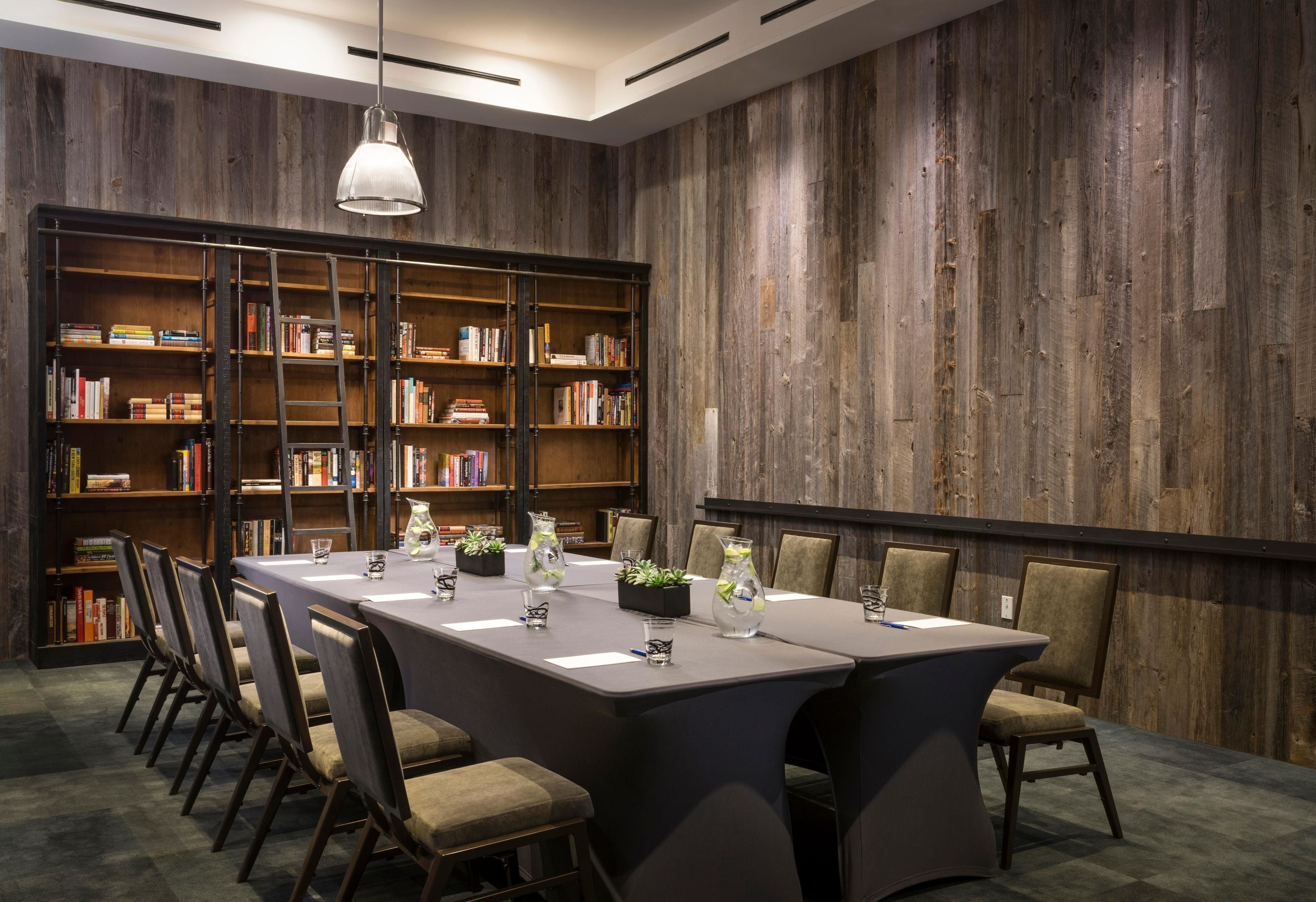 A conference room with a long table, chairs, bookshelves, and a hanging light fixture.