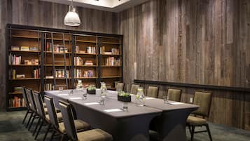 Un salón de conferencias con una larga mesa, sillas, estanterías y una lámpara colgante.