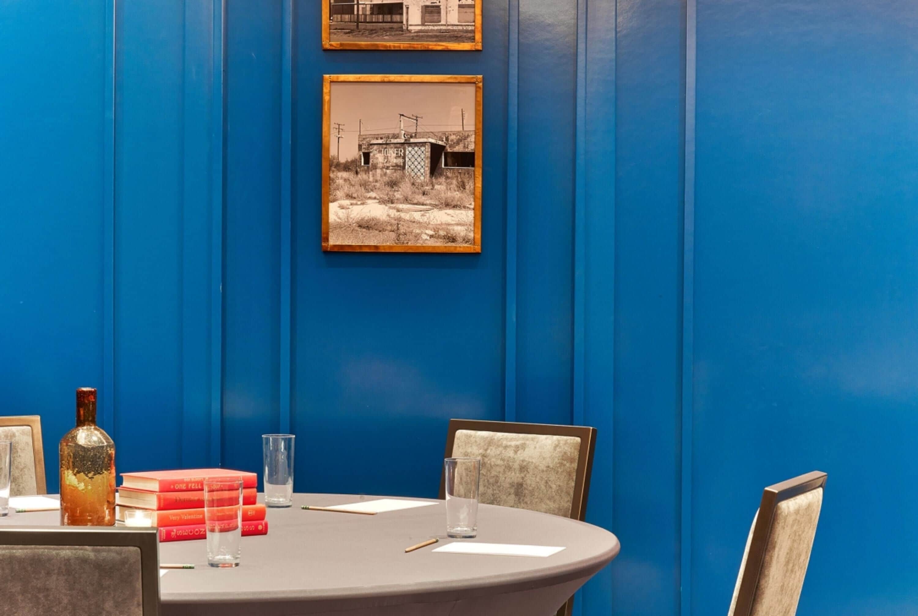 Une salle de conférence avec un mur bleu, une table ronde, des chaises, une bouteille et des livres.