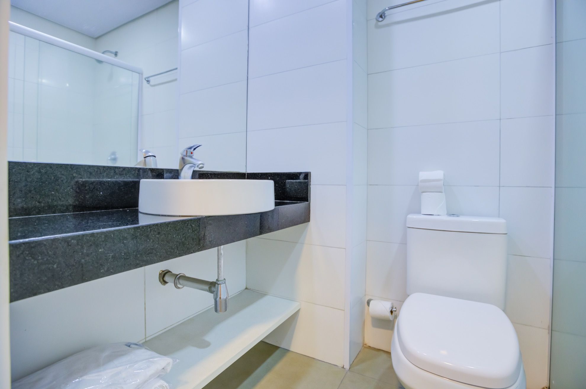 Un baño con inodoro blanco, lavamanos con grifo y espejo sobre el lavamanos.