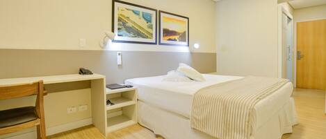 Een hotelkamer met een bed, een bureau met stoel, een nachtkastje en twee wandlampen.