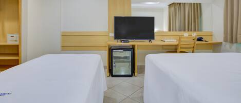 A hotel room with two beds, a desk with a television, a mini-fridge, and a chair.