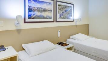 Una habitación de hotel con dos camas, una mesita de noche con teléfono y dos cuadros en la pared.
