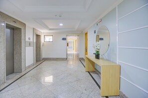 Un pasillo de hotel con suelo de mármol, un mostrador de recepción con espejo, y una puerta que da a un pasillo.