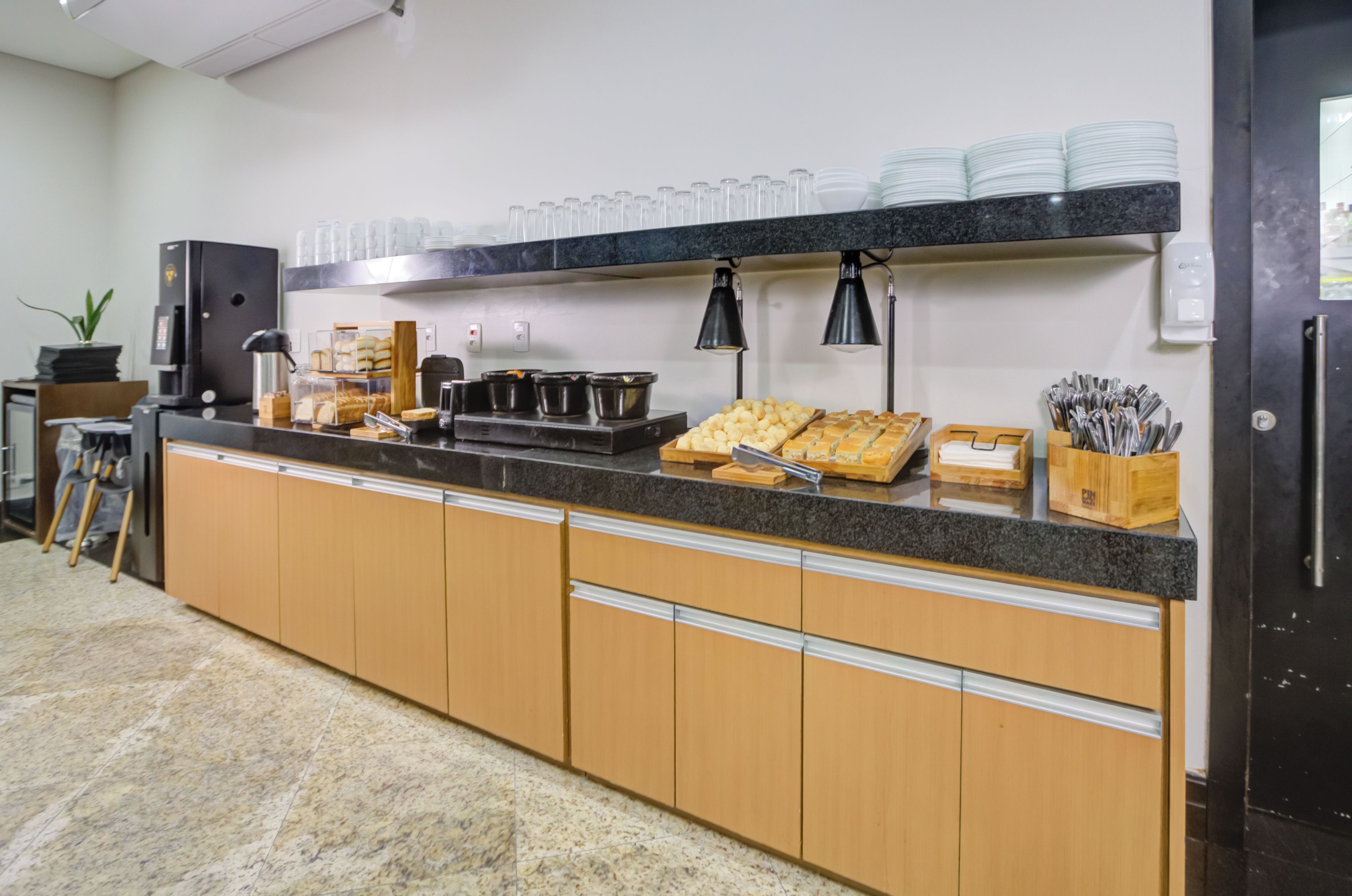 A kitchen with a marble countertop, wooden cabinets, a coffee machine, and various food items.