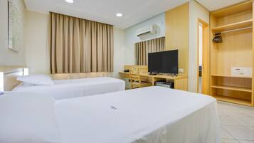 A hotel room with two beds, a desk with a television, an air conditioning unit, and a wooden wardrobe.