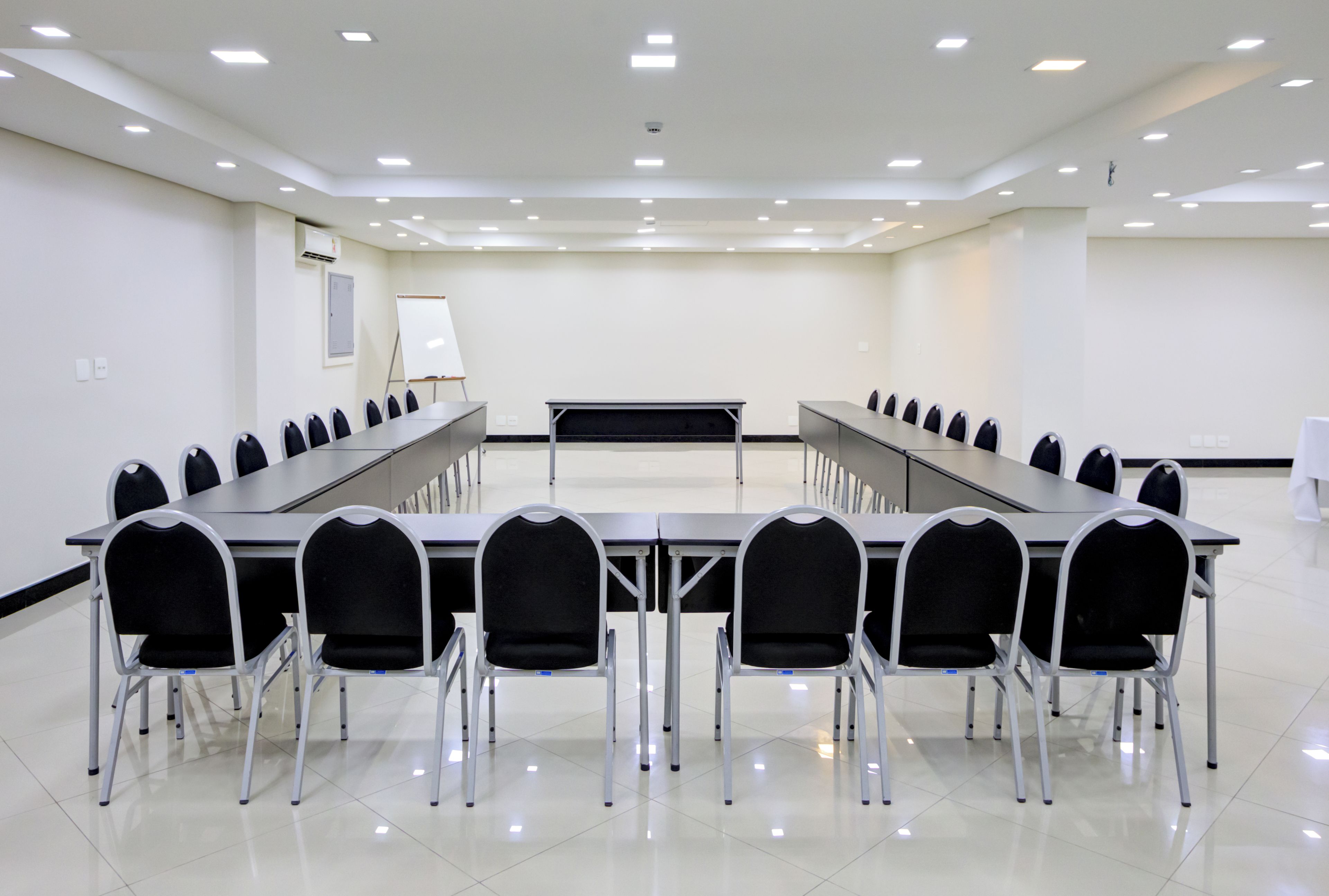 Un salón de conferencias con una larga mesa, varias sillas, una pizarra y un techo con iluminación empotrada.