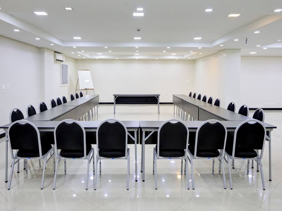 Un salón de conferencias con una larga mesa, varias sillas, una pizarra y un techo con iluminación empotrada.