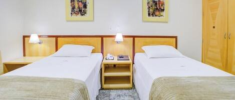 Habitación de hotel con dos camas individuales, un armario de madera y dos lámparas fijadas a la pared.