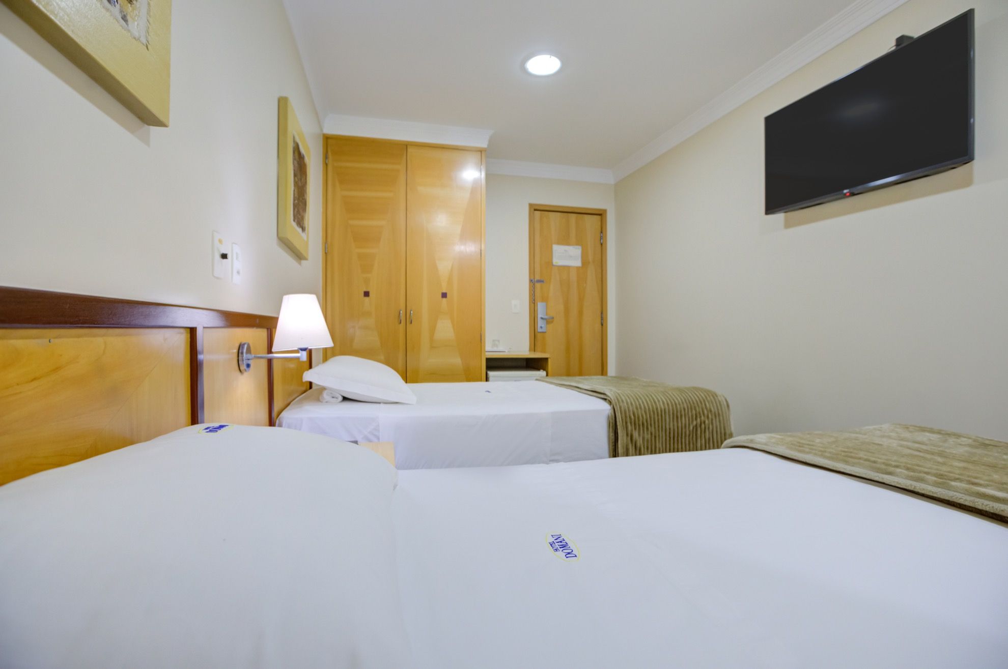 A hotel room with two beds, a television mounted on the wall, and a wooden wardrobe.