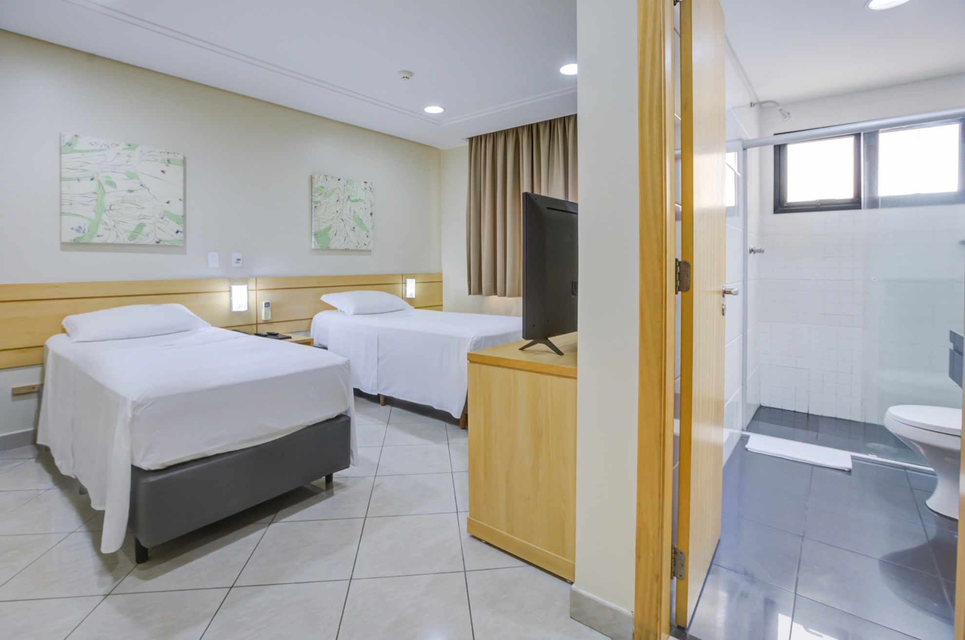 A hotel room with two beds, a TV, a wooden desk, and a bathroom with a toilet and shower.