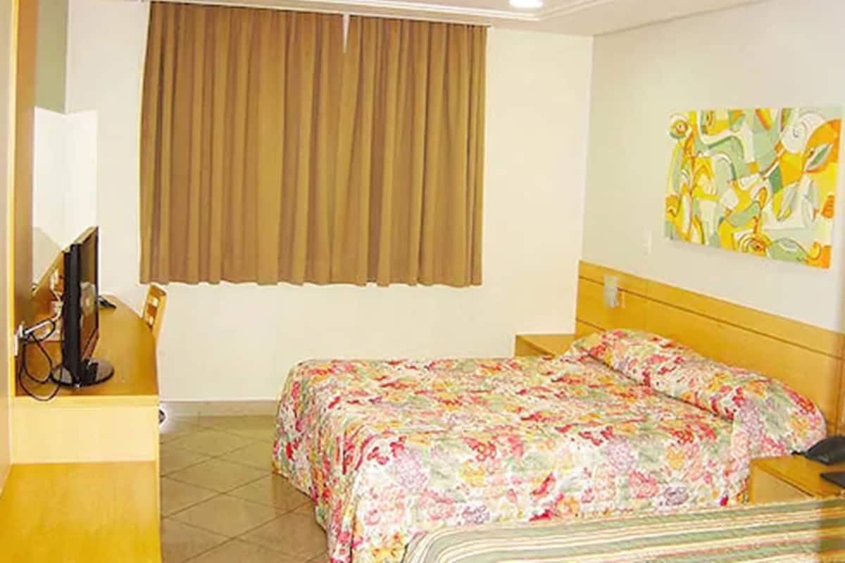 A hotel room with a bed, a desk with a computer, a television, and a painting on the wall.