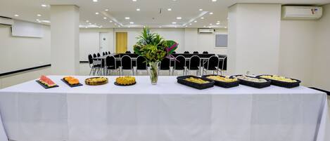Un salón de conferencias con una larga mesa dispuesta para una reunión, equipado con sillas y un mantel blanco.