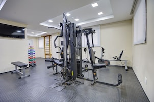Un gimnasio con equipos de ejercicio variados, un televisor en la pared y un zapatero.