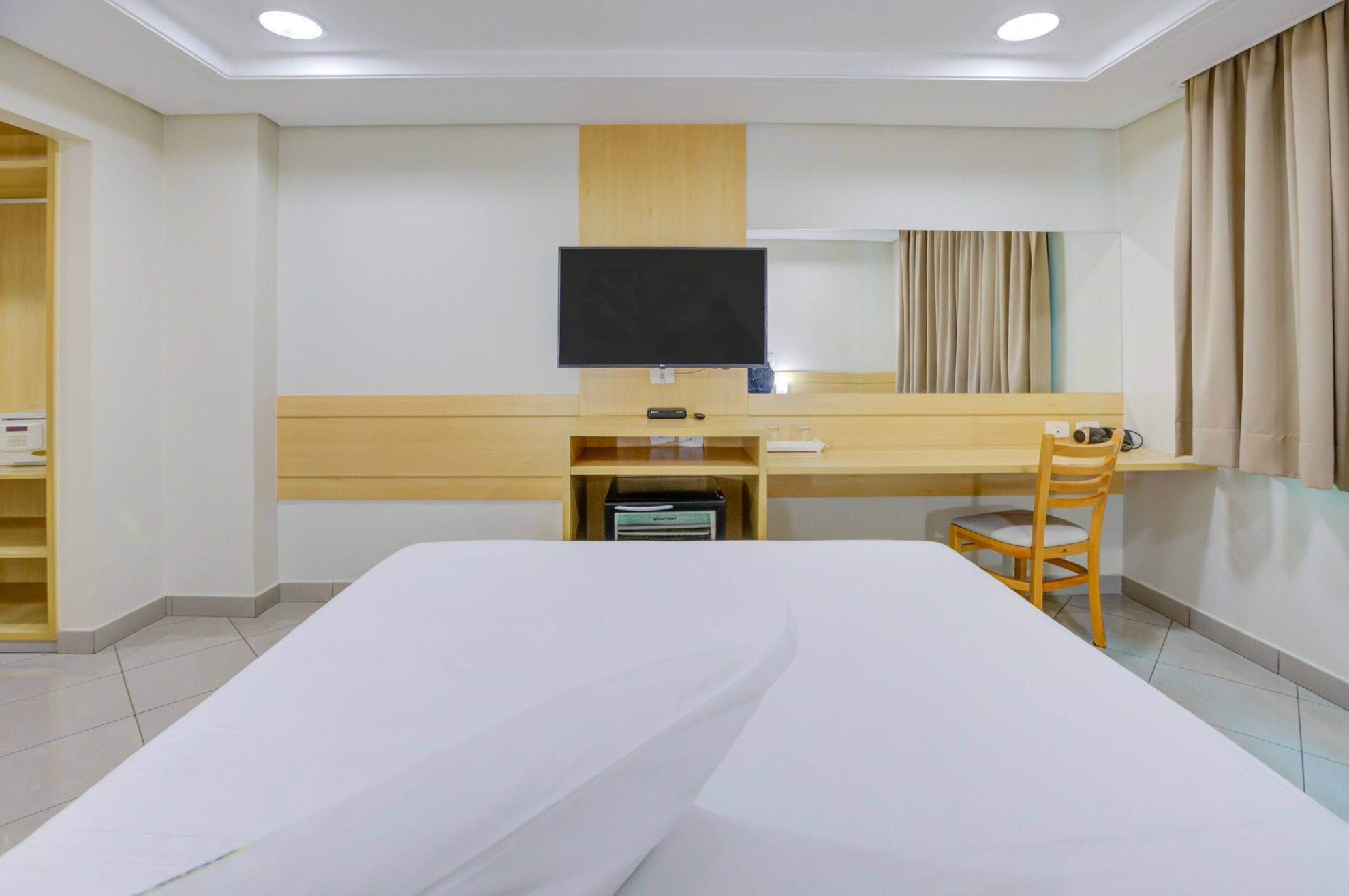 A hotel room with a bed, a desk, a chair, a television, and a window with curtains.