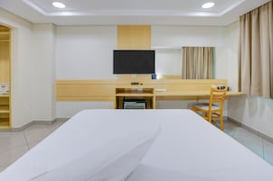 Habitación de hotel con cama, escritorio, silla, televisor y ventana con cortinas.