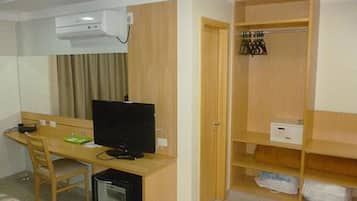 Une chambre d’hôtel de taille réduite, équipée d’un bureau, d’une chaise, d’une télévision et d’une armoire avec espace pour suspendre les vêtements.