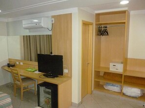 A compact hotel room with a desk, chair, television, and a wardrobe with hanging space. - Hotel Domani (Guarulhos)