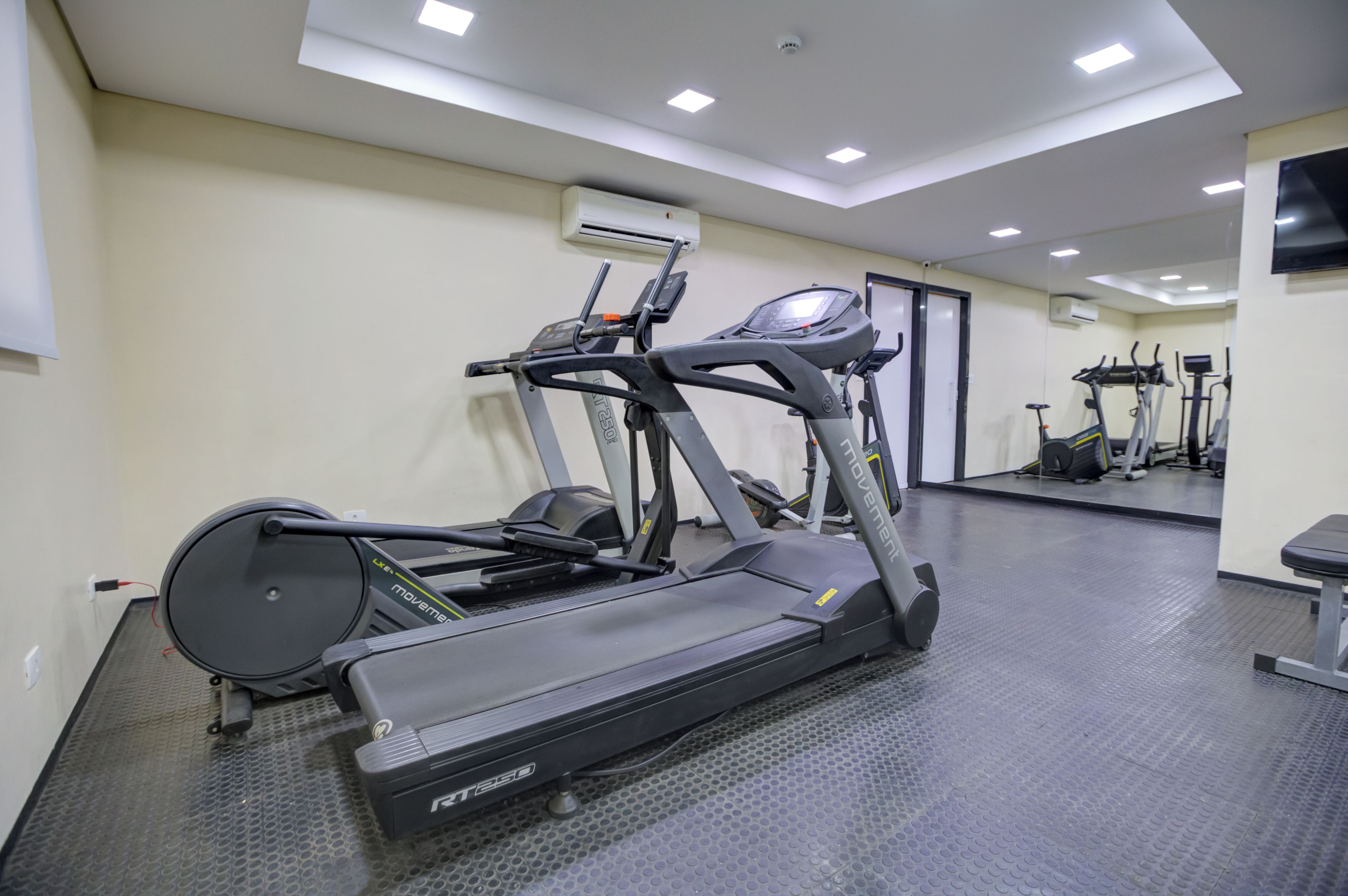 Une salle de sport équipée de tapis de course, de vélos d’appartement et d’un mur recouvert de miroirs.