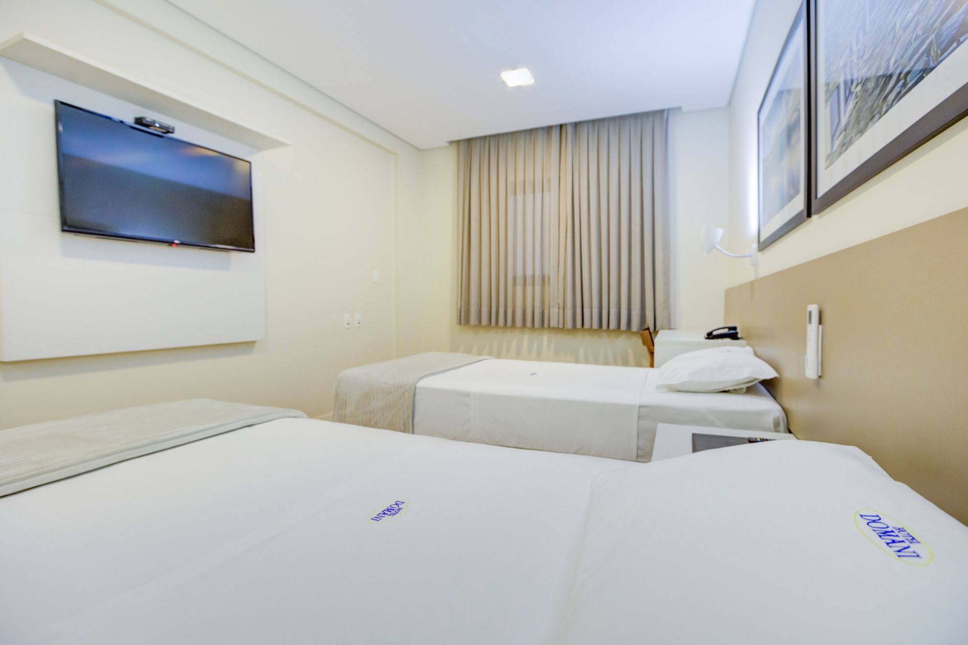 Habitación de hotel con dos camas, un televisor montado en la pared y una ventana con cortinas.