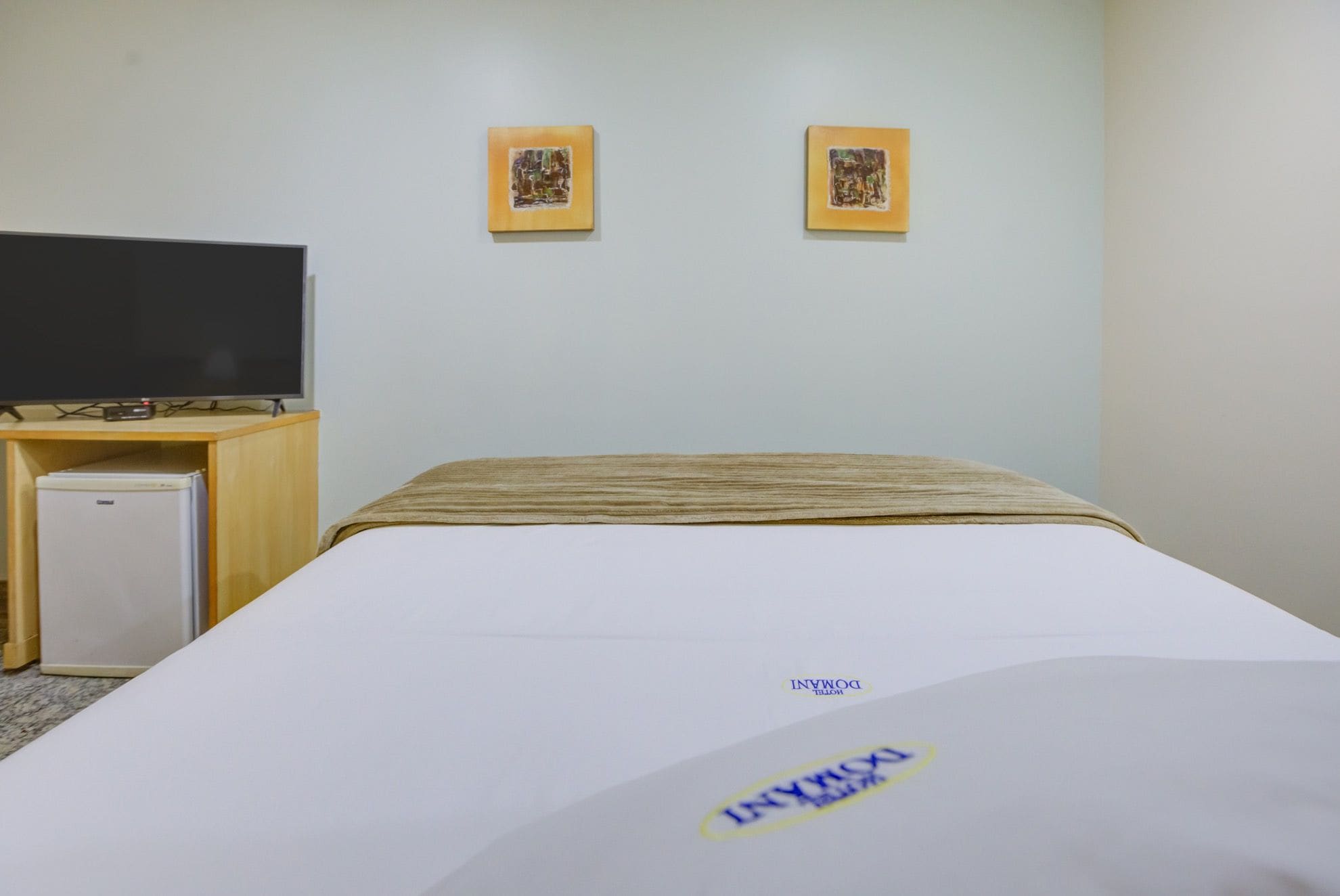 Ein Hotelzimmer mit einem Bett, einem Fernseher und zwei gerahmten Bildern an der Wand.