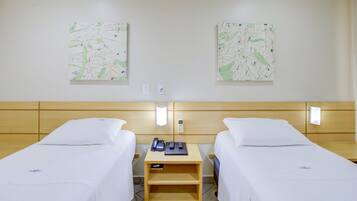 Habitación de hotel con dos camas individuales, una mesita de noche de madera con un teléfono y controles remotos, y dos obras de arte abstracto en la pared.