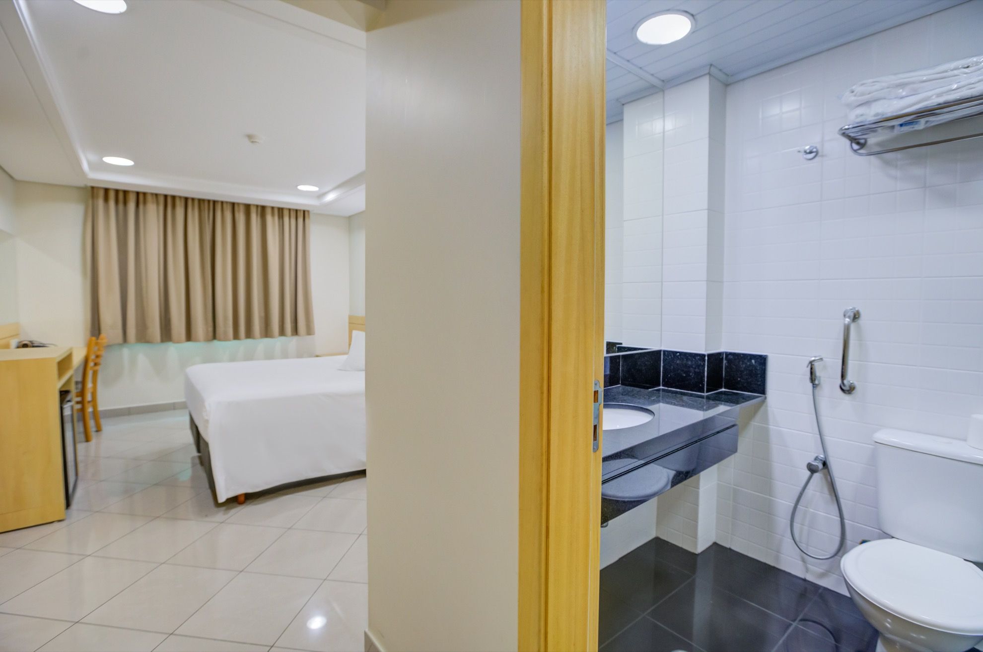 Habitación de hotel con cama, escritorio, baño con lavamanos, inodoro y ducha.