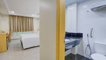 Habitación de hotel con cama, escritorio, baño con lavamanos, inodoro y ducha.