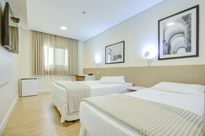 Une chambre d’hôtel avec deux lits, un bureau, une chaise, une petite table et un téléviseur fixé au mur.