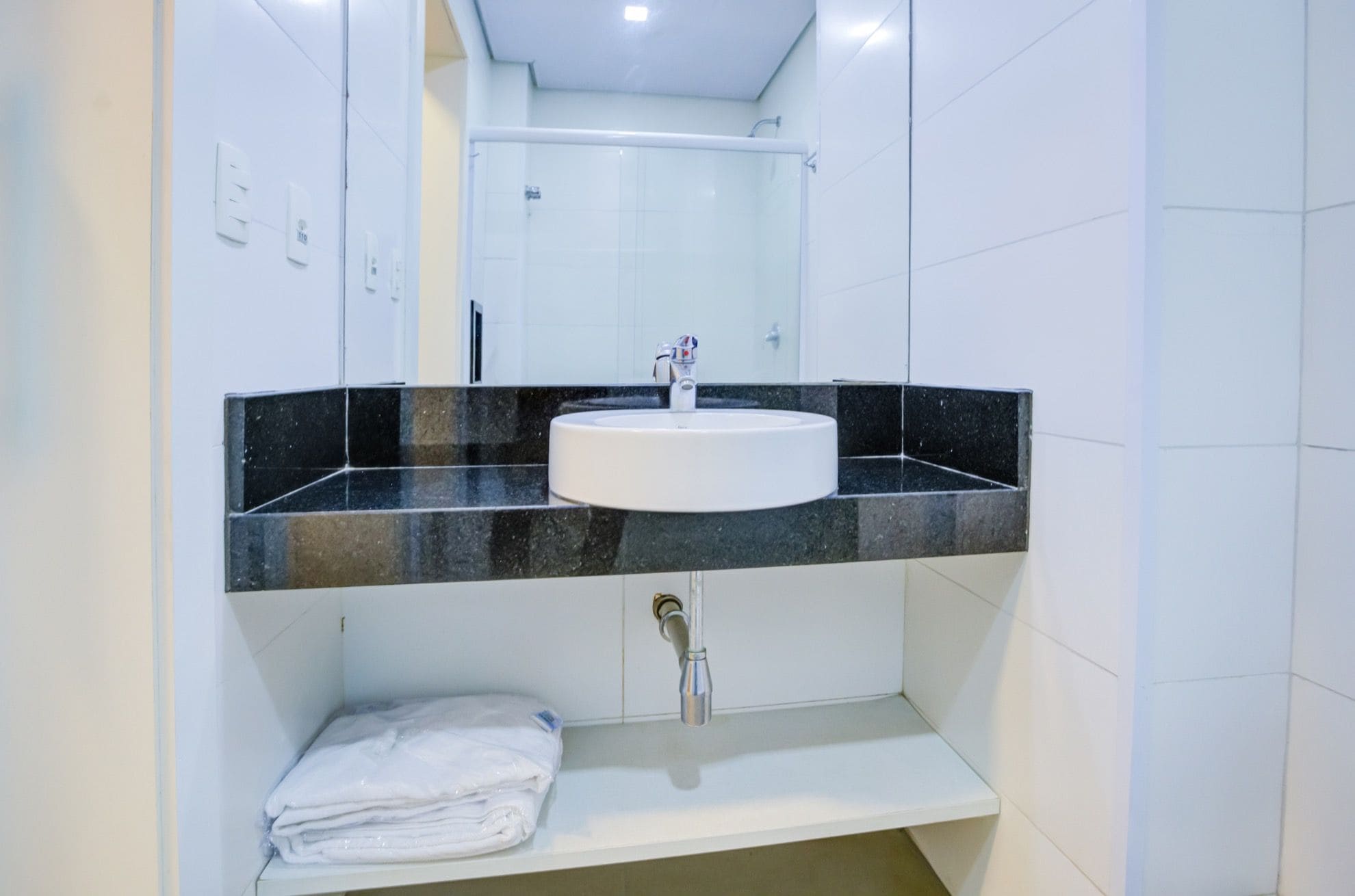 A bathroom with a white sink, black countertop, and a mirror above it.