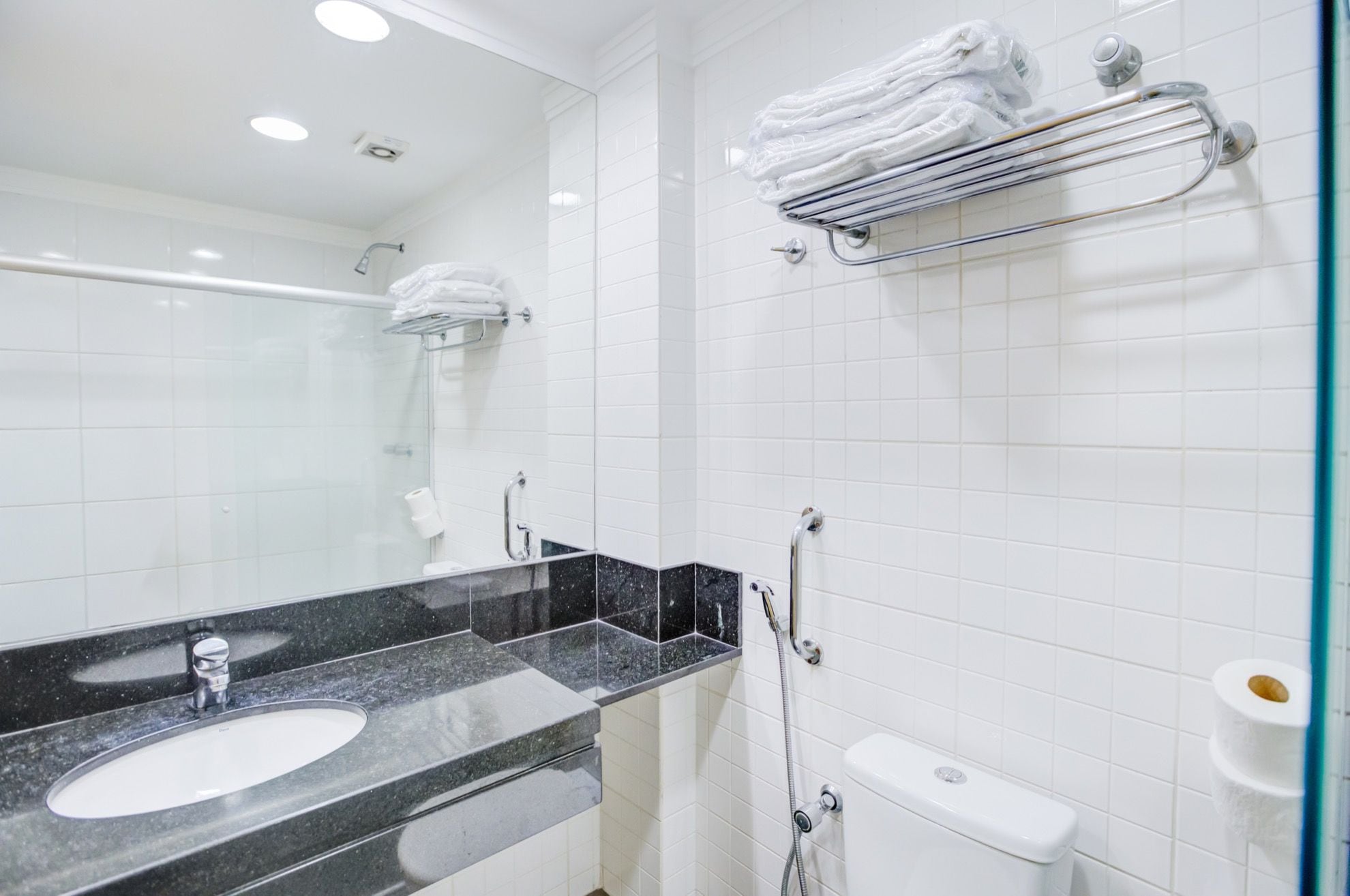 A modern bathroom with a black granite sink, white tiled walls, a glass shower enclosure, and a towel rack with folded towels.
