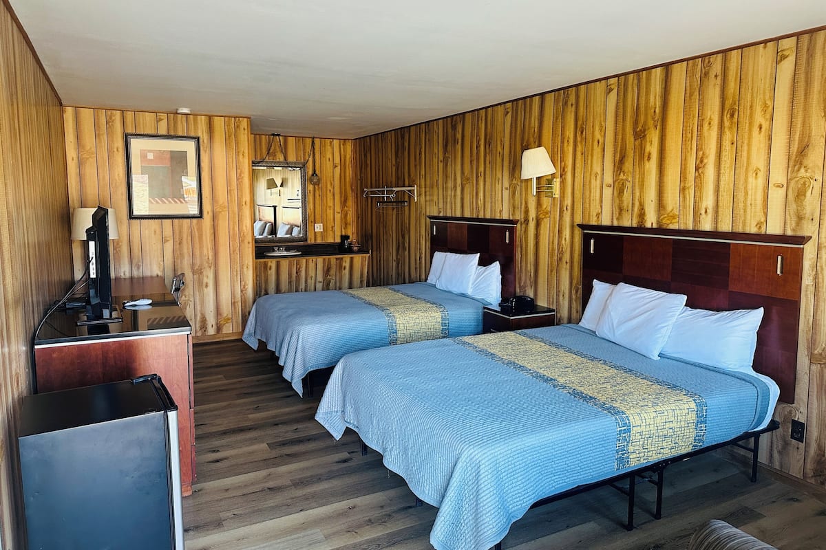A room with two beds, a desk, a television, and a mirror.