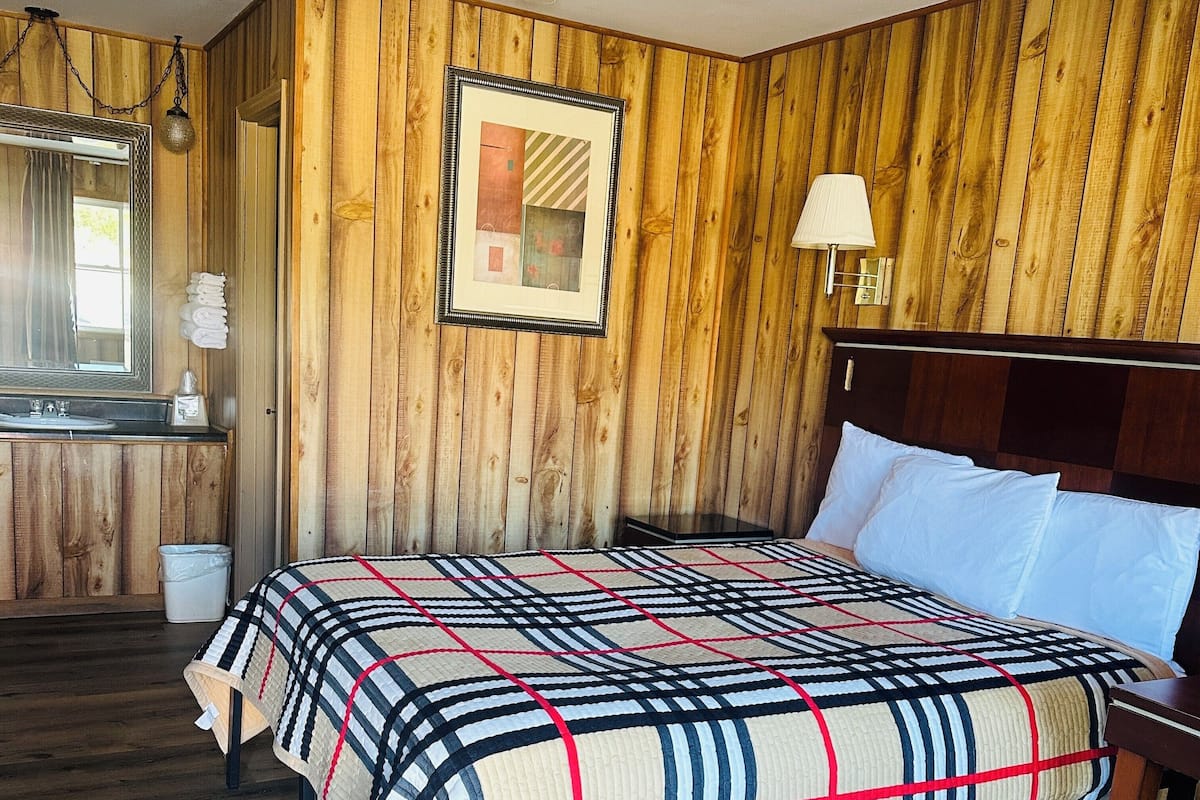 A wooden-paneled bedroom with a bed, a nightstand, a lamp, and a framed picture on the wall.