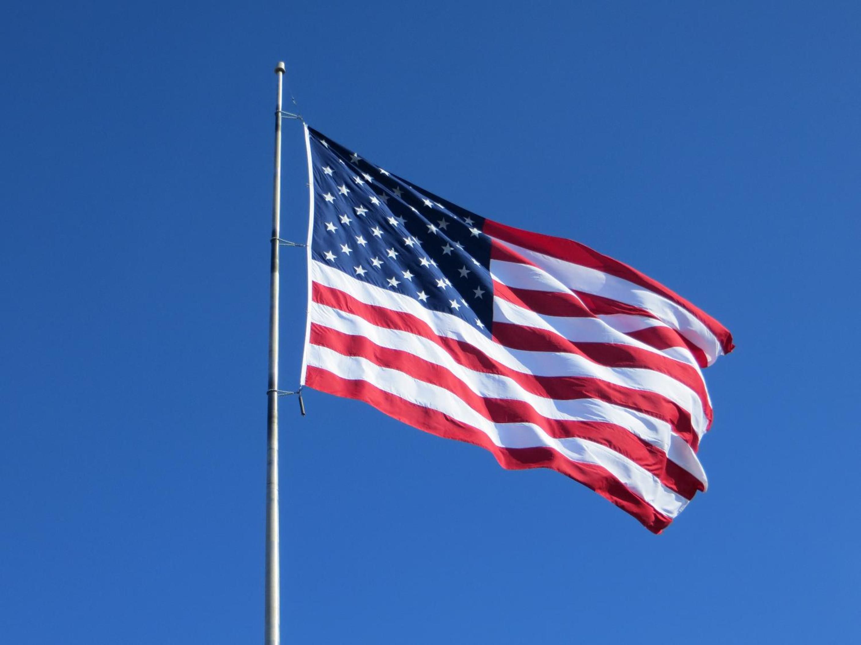 An American flag on a flagpole against a clear blue sky.