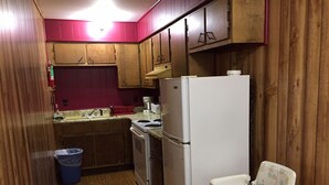 A compact kitchen with wooden cabinets, a white refrigerator, a small sink, and a child's high chair. - Country Inn Motel (Licking)