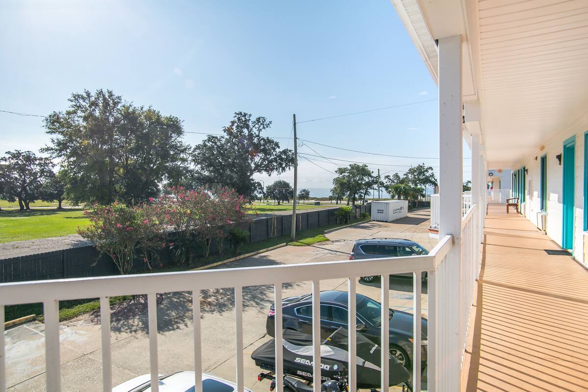 A view from a balcony overlooking a parking area with cars and a grassy area.