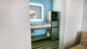 A compact kitchen with a built-in microwave, a refrigerator, and a sink with a granite countertop.