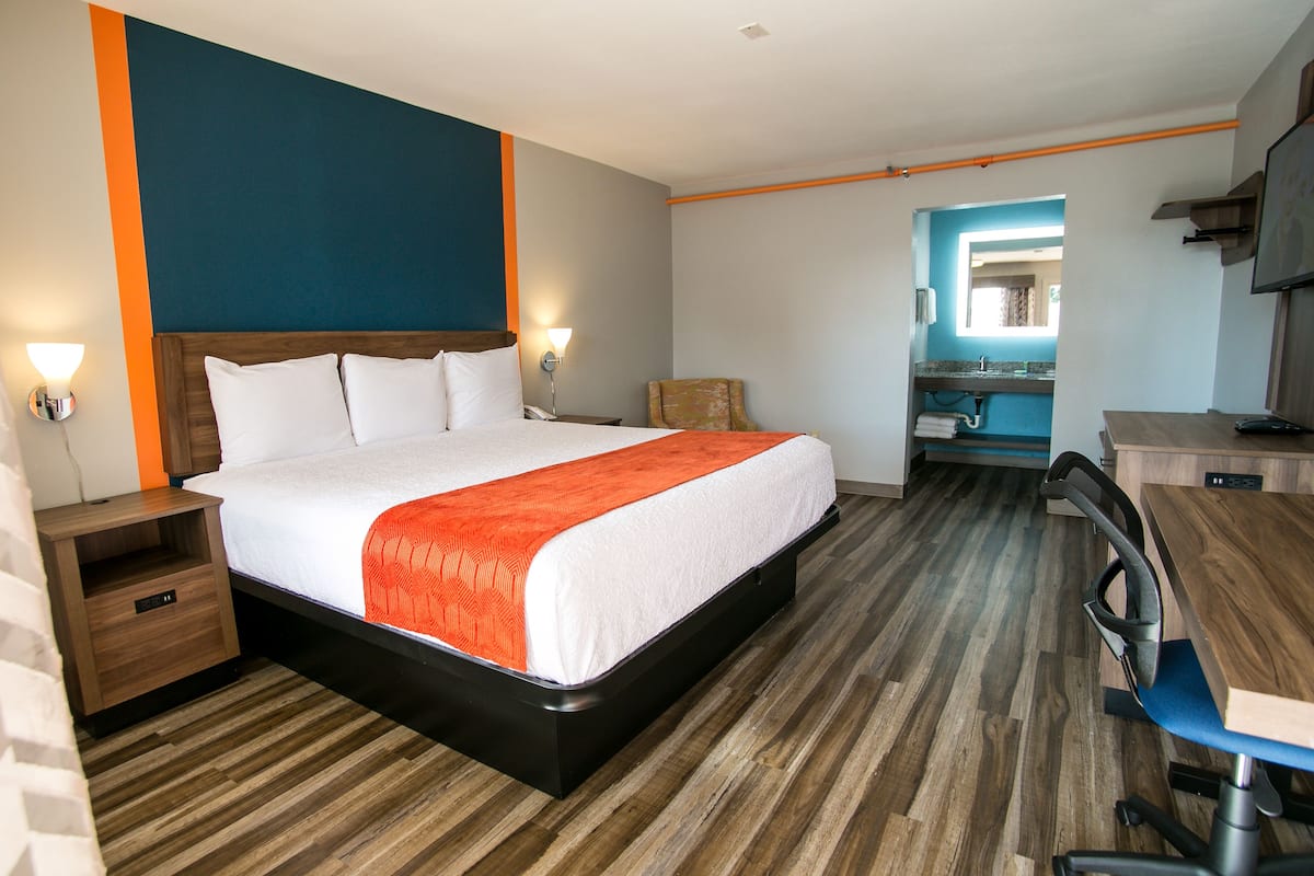 A hotel room with a bed, a desk, and a bathroom visible through an open doorway.