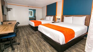 A hotel room with two beds, a desk, and a chair.