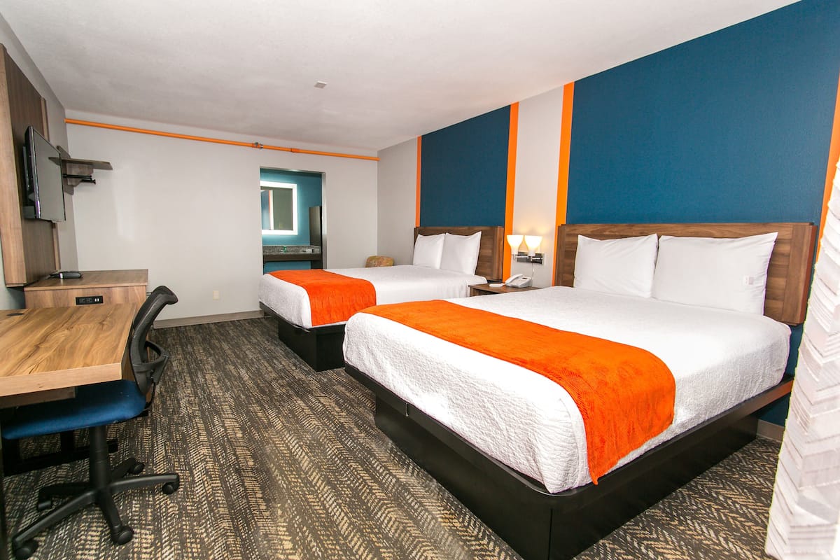 A hotel room with two beds, a desk, and a chair.
