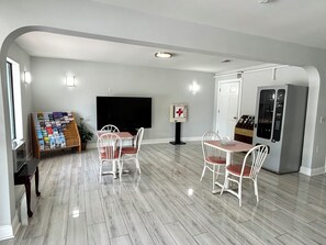 A modern living room with a flat-screen TV, a coffee machine, and a dining area with white chairs.