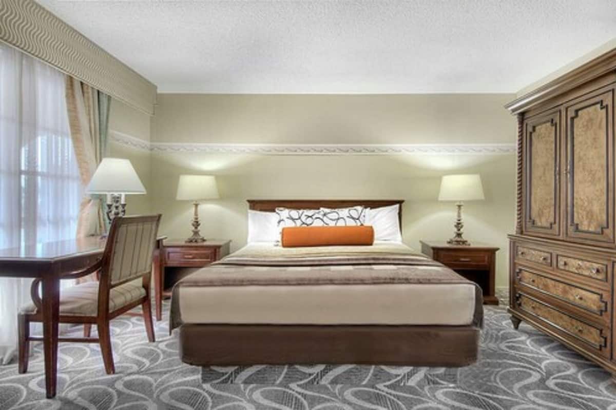 Una habitación de hotel con una cama grande, dos mesitas de noche con lámparas, un aparador de madera y una alfombra estampada.